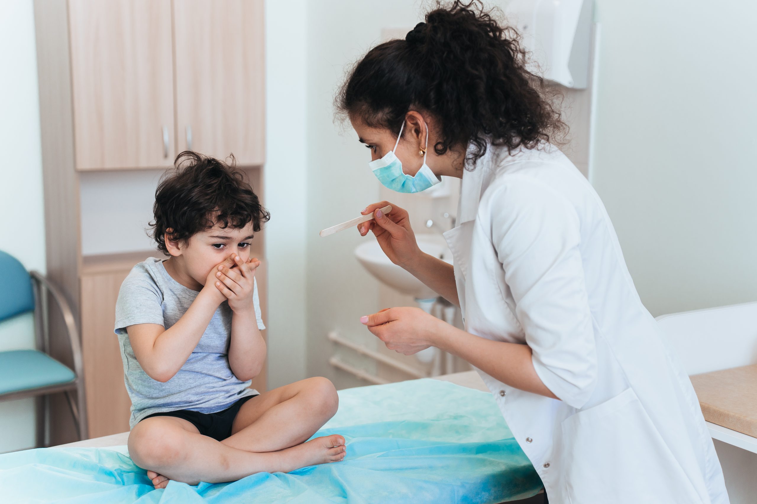Pediatrician using tongue depressor on young boy